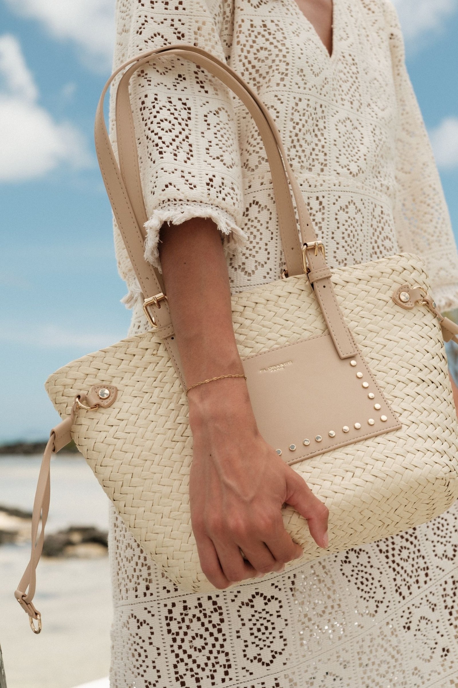 Vue de face du sac à main en paille beige avec hanse beige taupe, tenu par la main droite de la mannequin de profil au niveau de la hanche.